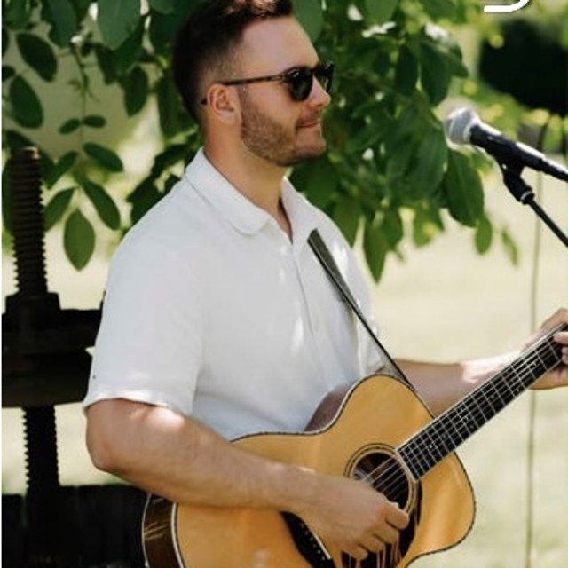 Dennis Ross mit Gitarre am Mikrofon im Grünen